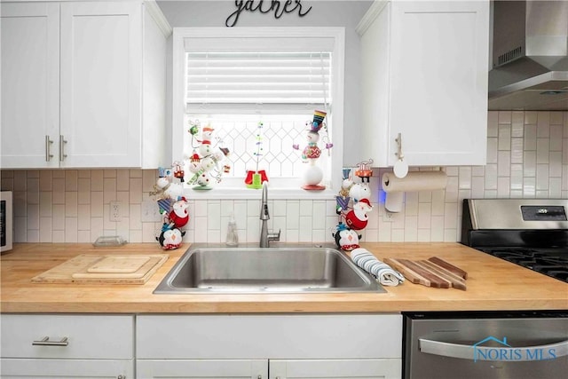 kitchen with wooden counters, a sink, white cabinets, appliances with stainless steel finishes, and wall chimney range hood