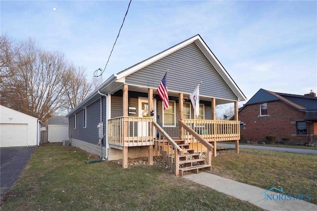 bungalow featuring a porch, an outdoor structure, a detached garage, and a front lawn