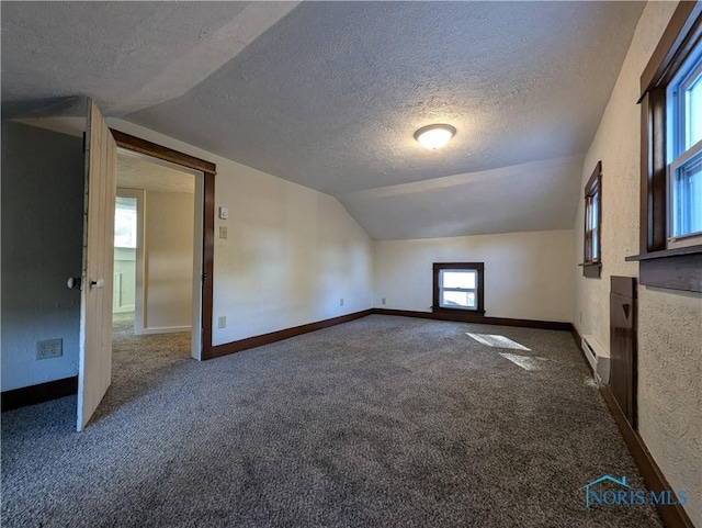 bonus room featuring a textured ceiling, dark carpet, baseboard heating, and lofted ceiling