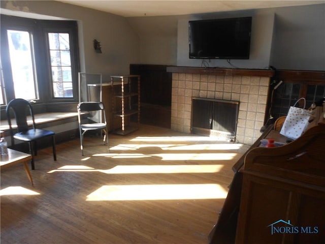 living area with a tiled fireplace, wood-type flooring, and vaulted ceiling