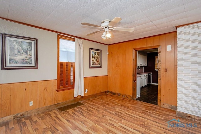 unfurnished room with wooden walls, light hardwood / wood-style floors, ceiling fan, and ornamental molding