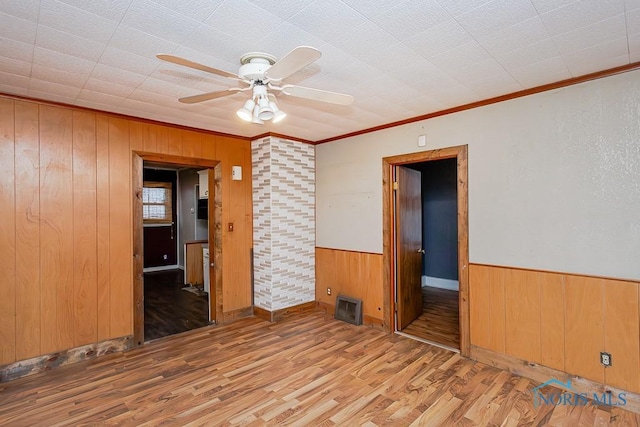 unfurnished room with light hardwood / wood-style flooring, ceiling fan, ornamental molding, and wood walls