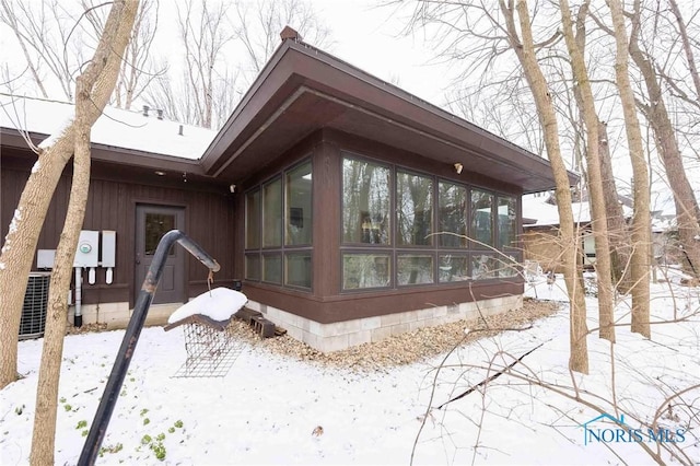 snow covered property featuring a sunroom and central air condition unit