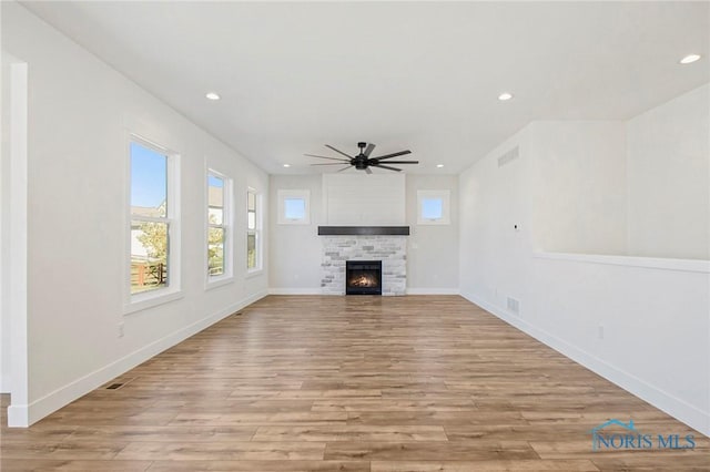 unfurnished living room featuring light hardwood / wood-style flooring, a stone fireplace, and ceiling fan