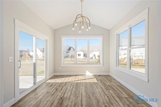 unfurnished dining area with an inviting chandelier, lofted ceiling, and light wood-type flooring