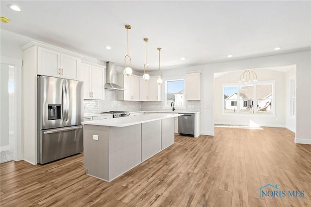 kitchen featuring a center island, white cabinets, hanging light fixtures, wall chimney exhaust hood, and stainless steel appliances