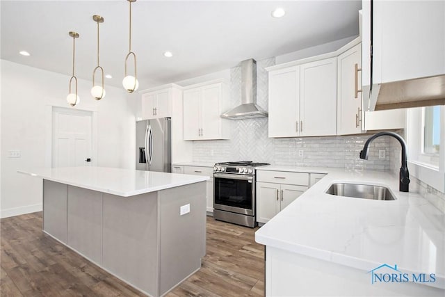 kitchen with sink, stainless steel appliances, wall chimney range hood, a kitchen island, and white cabinets