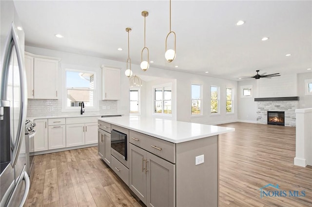 kitchen featuring appliances with stainless steel finishes, decorative light fixtures, white cabinets, a kitchen island, and a stone fireplace