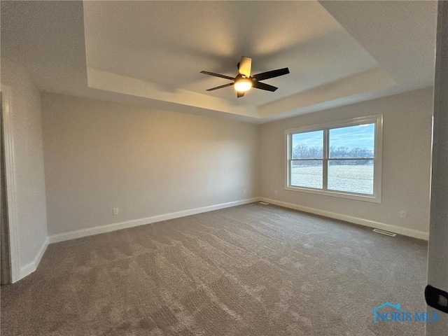 empty room featuring a raised ceiling, dark colored carpet, and ceiling fan