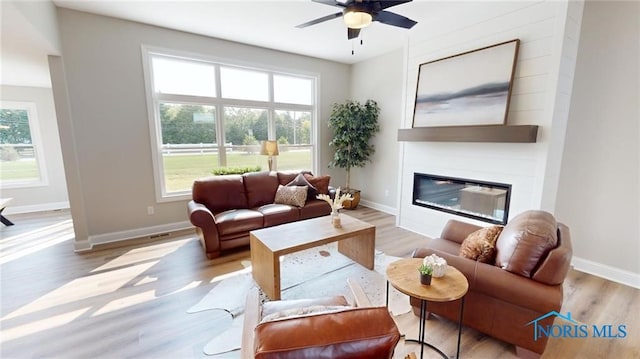 living room featuring light hardwood / wood-style flooring, ceiling fan, and a large fireplace