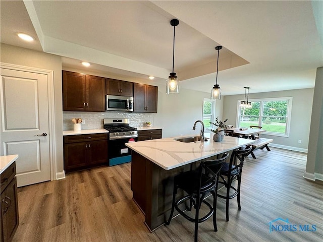 kitchen with light stone countertops, sink, pendant lighting, stainless steel appliances, and a center island with sink