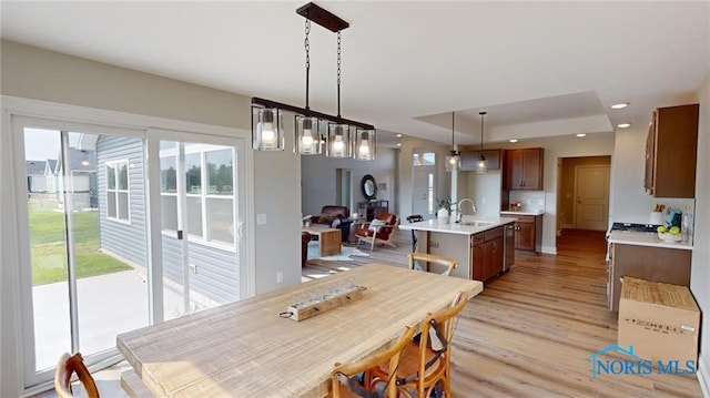 dining space with sink, light hardwood / wood-style floors, and a tray ceiling