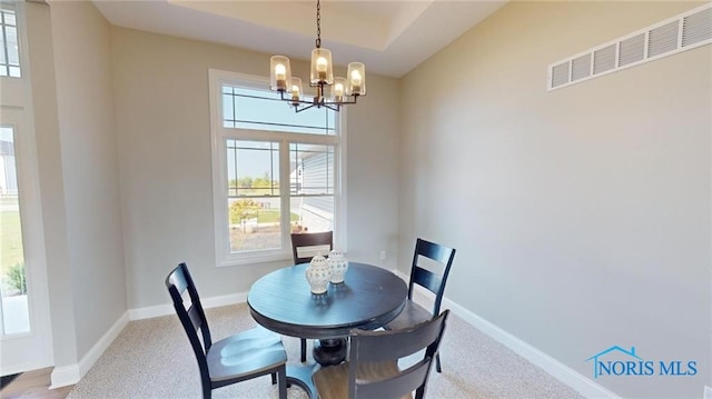 carpeted dining room featuring a raised ceiling and an inviting chandelier