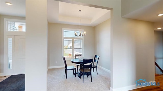 carpeted dining room with an inviting chandelier, a wealth of natural light, and a raised ceiling