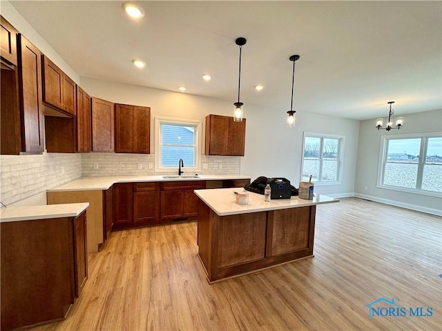 kitchen featuring a kitchen island, sink, a chandelier, hanging light fixtures, and light hardwood / wood-style flooring