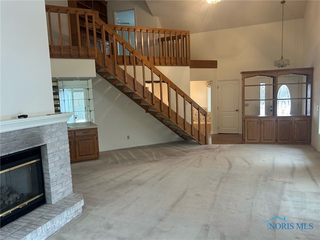 entryway featuring a chandelier, high vaulted ceiling, light colored carpet, and a brick fireplace