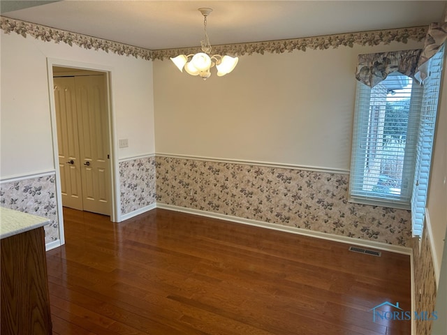 spare room with dark wood-type flooring and a chandelier