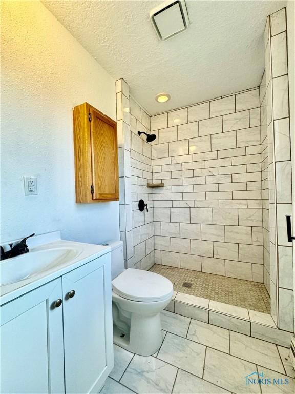 bathroom with toilet, vanity, a textured ceiling, and tiled shower