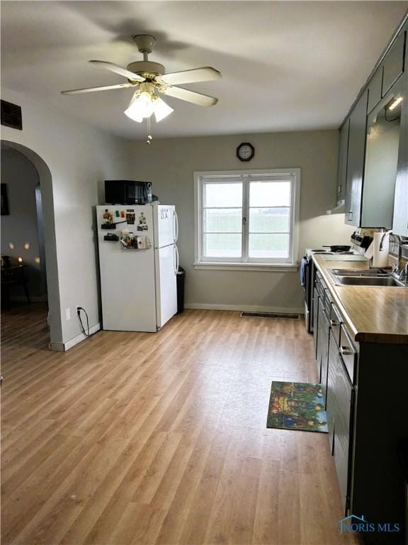 kitchen with white refrigerator, sink, ceiling fan, stainless steel range, and light hardwood / wood-style floors