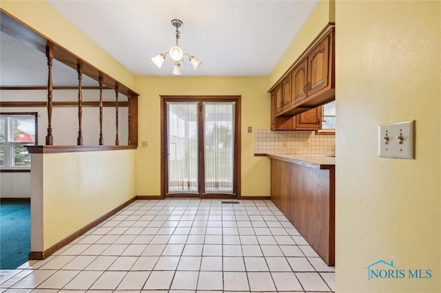 kitchen with decorative backsplash, light tile patterned floors, hanging light fixtures, and an inviting chandelier