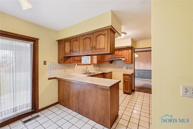 kitchen featuring kitchen peninsula, backsplash, sink, light tile patterned floors, and tile counters