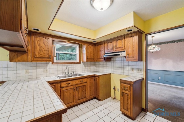 kitchen featuring light tile patterned flooring, an inviting chandelier, tile counters, and sink