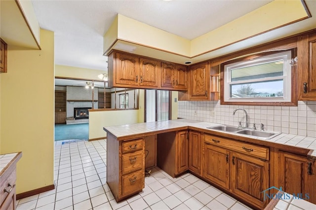 kitchen with kitchen peninsula, sink, light tile patterned floors, tile countertops, and a fireplace