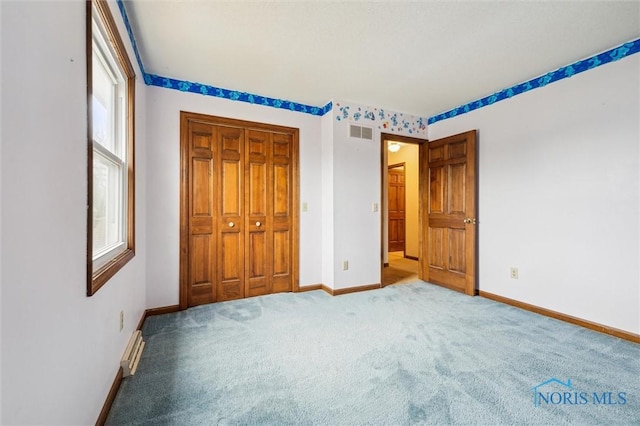 unfurnished bedroom with carpet floors, baseboard heating, and a closet