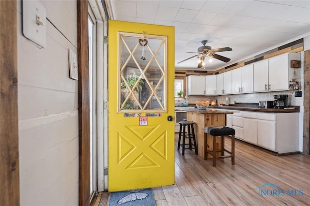 kitchen with white cabinetry, ceiling fan, a breakfast bar, decorative backsplash, and light hardwood / wood-style flooring