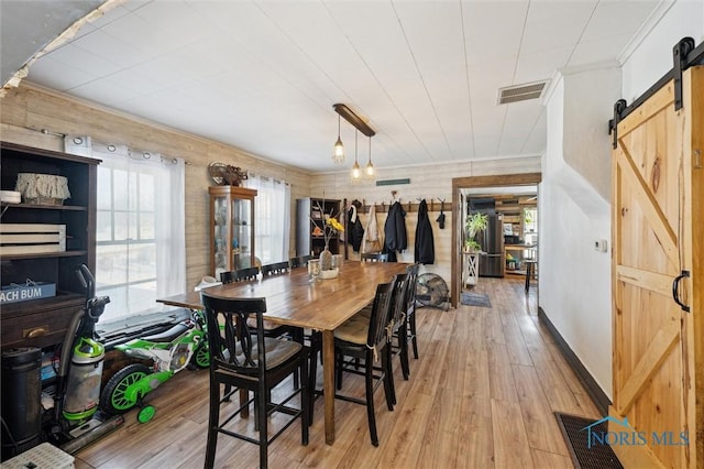 dining room with light wood-type flooring, wooden walls, and a barn door