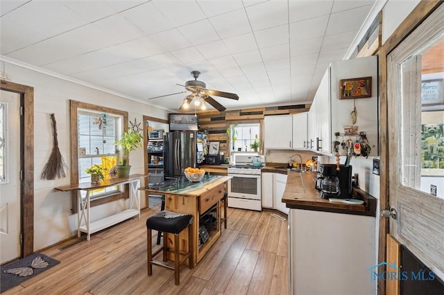 kitchen with butcher block countertops, white gas range oven, stainless steel refrigerator, and white cabinetry