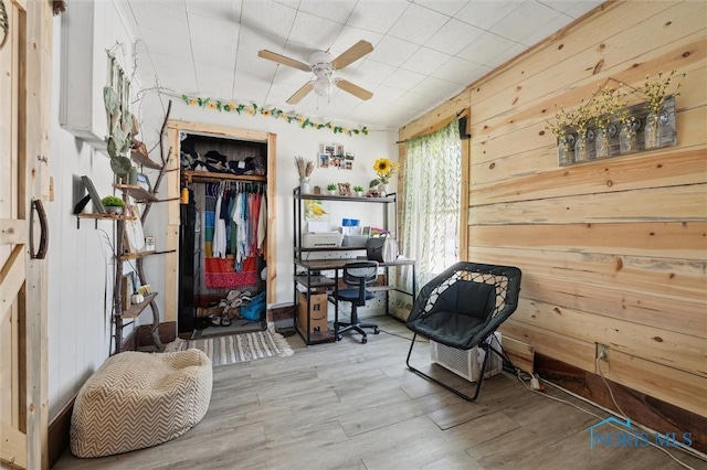 living area with ceiling fan, wood walls, and wood-type flooring