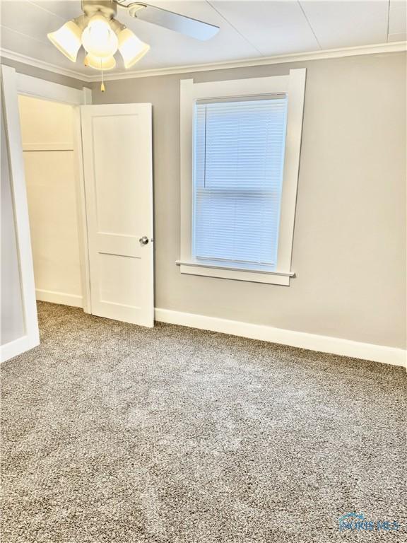 empty room with ceiling fan, ornamental molding, and carpet flooring