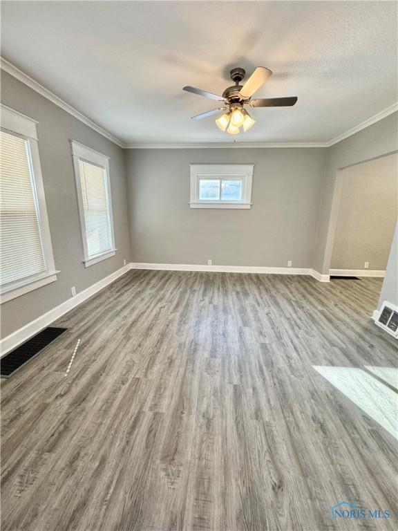 empty room featuring ceiling fan, wood-type flooring, ornamental molding, and a textured ceiling