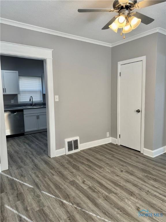 empty room featuring ceiling fan, dark hardwood / wood-style floors, sink, and crown molding