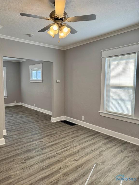 empty room featuring a textured ceiling, ceiling fan, ornamental molding, and hardwood / wood-style flooring