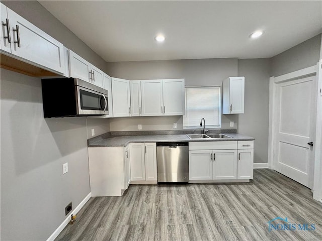 kitchen with light wood-type flooring, appliances with stainless steel finishes, white cabinets, and sink