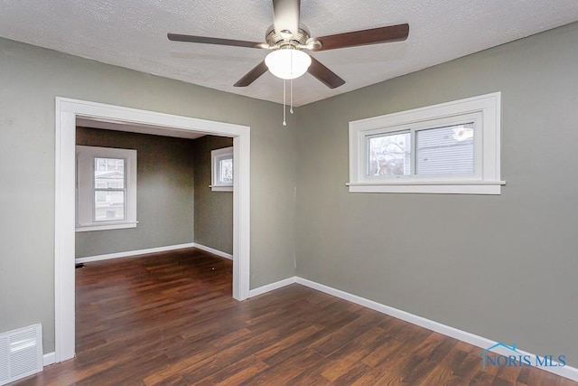 unfurnished room with a textured ceiling, ceiling fan, dark wood-type flooring, and a wealth of natural light