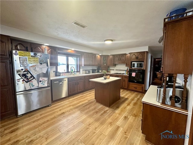 kitchen with sink, appliances with stainless steel finishes, dark brown cabinets, a kitchen island, and light wood-type flooring