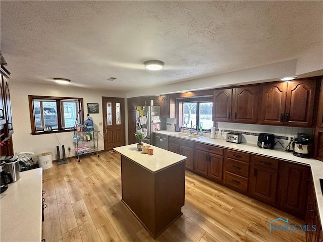 kitchen with sink, a center island, light hardwood / wood-style flooring, stainless steel fridge, and a textured ceiling