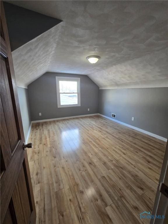 additional living space with vaulted ceiling, light hardwood / wood-style floors, and a textured ceiling