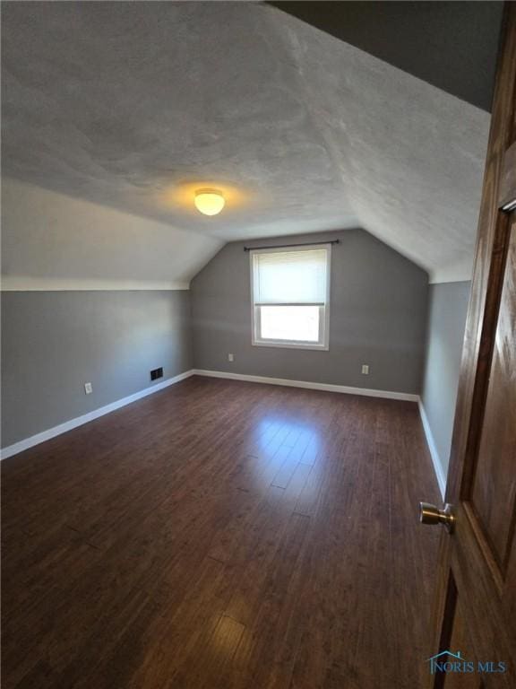 additional living space featuring dark wood-type flooring, vaulted ceiling, and a textured ceiling