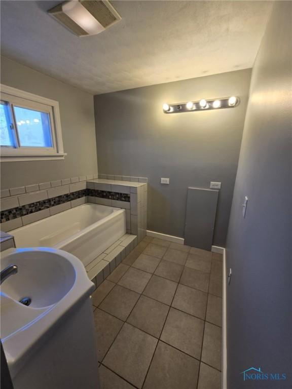 bathroom with a tub to relax in, tile patterned floors, and sink