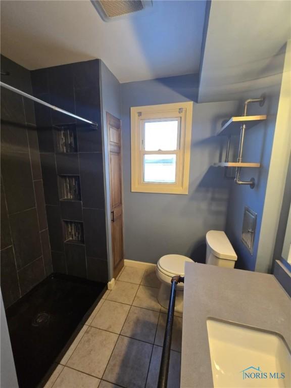 bathroom with tiled shower, sink, tile patterned floors, and toilet