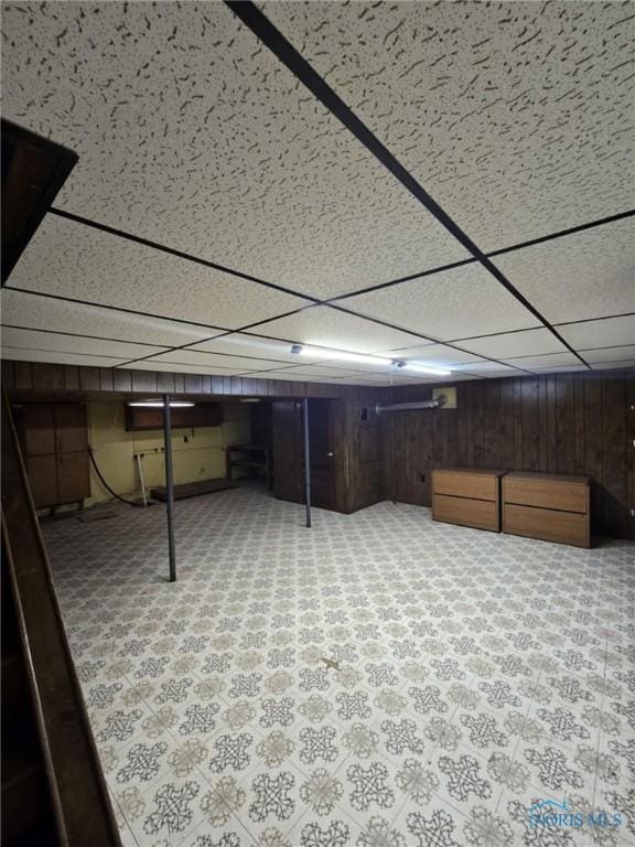 basement featuring a drop ceiling and wooden walls