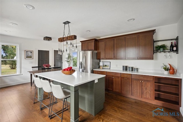 kitchen with a breakfast bar, dark wood-type flooring, stainless steel fridge with ice dispenser, a center island, and hanging light fixtures