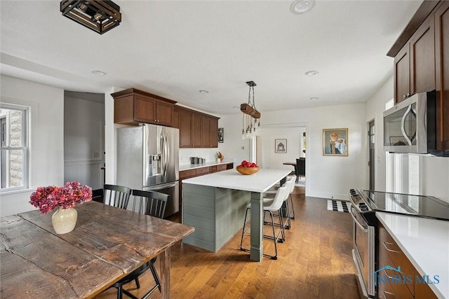 kitchen featuring hanging light fixtures, dark wood-type flooring, a breakfast bar area, a kitchen island, and appliances with stainless steel finishes