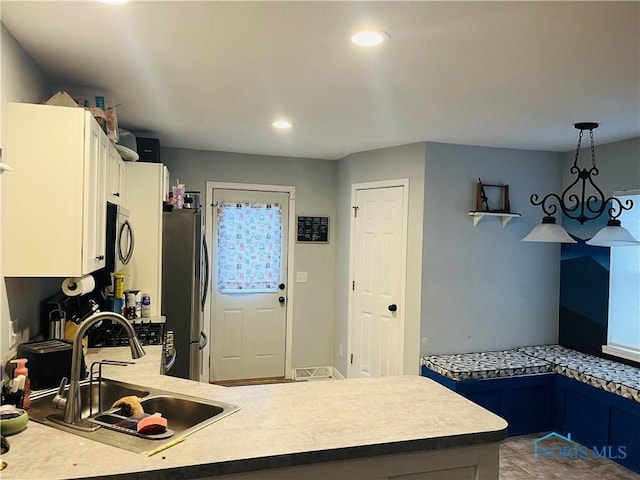 kitchen featuring pendant lighting, blue cabinets, sink, stainless steel fridge, and kitchen peninsula