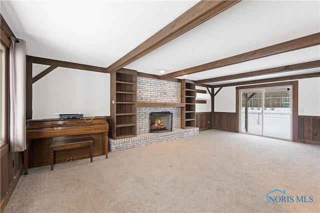 living room with wood walls, carpet flooring, built in features, a fireplace, and beam ceiling