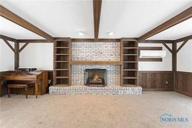 carpeted living room with a wall mounted air conditioner, built in shelves, a textured ceiling, beamed ceiling, and a fireplace